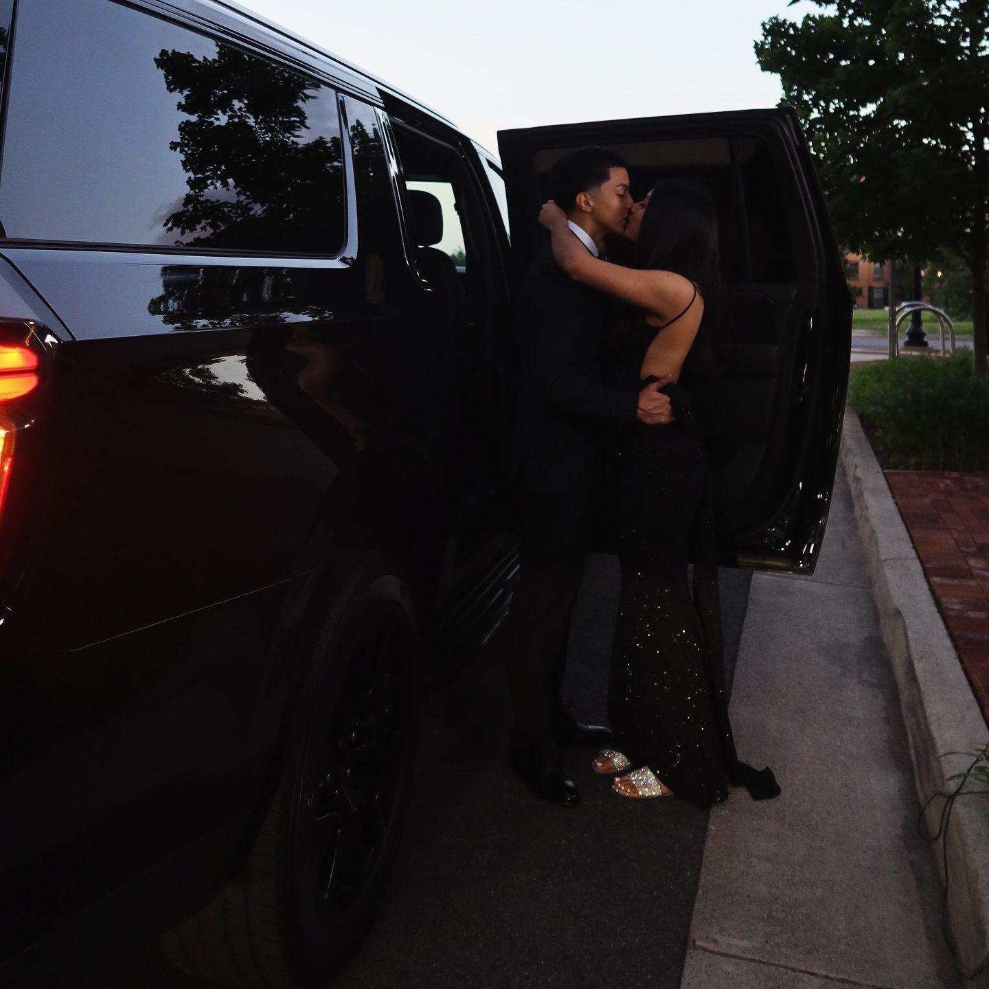 Two guests in suits beside a black SUV in warm evening light